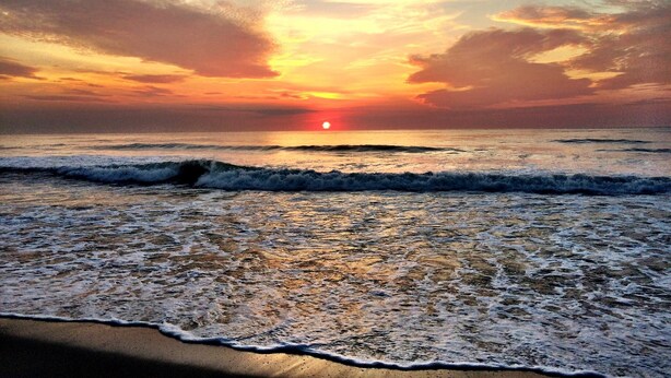 Una playa con olas y un atardecer.