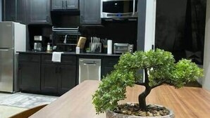 A modern kitchen with dark cabinetry, stainless steel appliances, and a central island with a bonsai tree. - Eva's Zen House | 2BR/2BA | Near Mercedes-Benz (Atlanta)