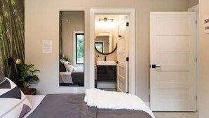 A bedroom with a bed, a mirror, a door, and a view into another room. - Eva's Zen House | 2BR/2BA | Near Mercedes-Benz (Atlanta)