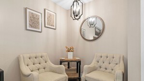 A room with two tufted armchairs, a small table with a vase, framed botanical prints, and a round mirror on the wall. - SADIE'S COTTAGE - Private Hot Tub and Fire Pit (Branson)