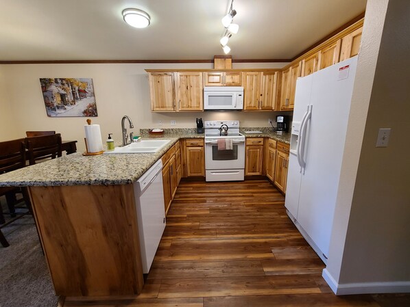 A kitchen with wooden cabinets, a granite countertop, a built-in oven, a microwave, and a refrigerator.
