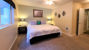 A bedroom with a bed, two bedside lamps, a ceiling fan, a window with curtains, and a door. - The Perfect Place (Leavenworth)