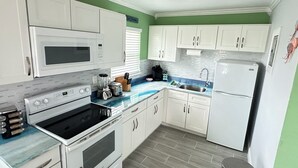 Una cocina compacta con armarios blancos, microondas integrado, estufa y lavamanos.