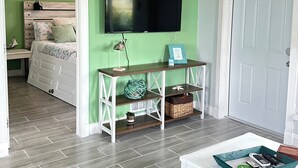 Un dormitorio con una cama, un televisor montado en la pared, una consola de madera y una puerta.
