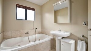 A bathroom with a bathtub, a sink, and a window with a blind. - Heritage Villa 5 (Wanaka)