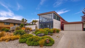 A modern two-story house with a garage, surrounded by landscaped garden with various shrubs and plants.