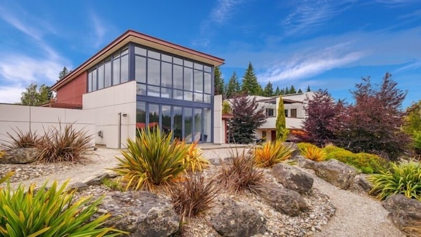 A modern house with a glass facade, surrounded by landscaped gardens with various plants and rocks.