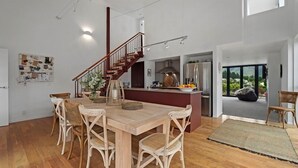A spacious dining area with a wooden table and wicker chairs, a kitchen with modern appliances, and a staircase leading to an upper level.