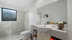 A modern bathroom with a glass shower enclosure, a toilet, a sink with a mirror, and a potted plant.