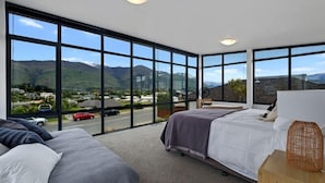 A bedroom with a large window offering a mountain view, a bed, and a bedside table.