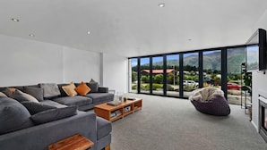 A modern living room with a grey sofa, a wooden coffee table, and a large window offering a mountain view.
