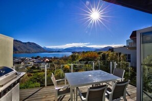 Un balcón con vista despejada a un lago y montañas, una parrilla y una mesa de comedor con sillas.