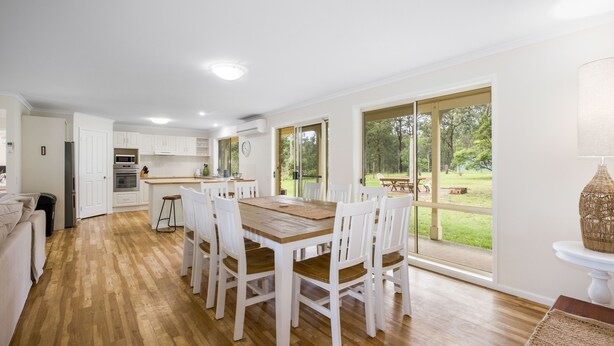 A spacious kitchen with white cabinets, a wooden dining table, and large sliding glass doors leading to a garden. - Bundara- Hunter Valley Retreat | Sleeps 11 | Rural | Resting amongst the trees (Congewai)