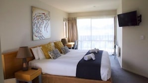 Une chambre d’hôtel avec un grand lit, un téléviseur à écran plat fixé au mur, un tableau au-dessus du lit et une fenêtre avec des rideaux.