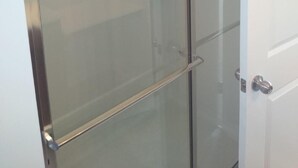 A glass-enclosed shower stall with a stainless steel frame and a white door.