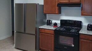 A kitchen with a stainless steel refrigerator, a black stove, wooden cabinets, and a granite countertop.