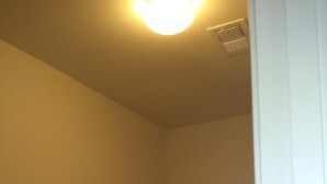 A small, dimly lit closet with a single hanging rod and a light fixture on the ceiling.