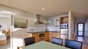 A modern kitchen with wooden cabinets, stainless steel appliances, and a dining area with a glass table and chairs. - Rocky Mountain Apartment - 111-112 (Wanaka)