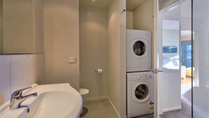 A modern bathroom with a sink, toilet, and stacked washing machines. - Rocky Mountain Apartment - 111-112 (Wanaka)
