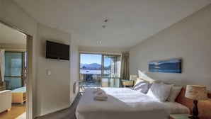 A hotel room with a large bed, a television, a painting, and a view of the mountains through the window. - Rocky Mountain Apartment - 111-112 (Wanaka)
