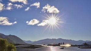A clear sky with the sun shining, mountains in the background, and solar panels on rooftops. - Rocky Mountain Apartment - 111-112 (Wanaka)