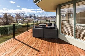 A wooden deck with a dark grey sofa and a glass enclosure. - Ultimate Escapes (Wanaka)
