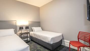 Habitación de hotel con dos camas, una mesita de noche con lámparas, una silla roja y un televisor montado en la pared.