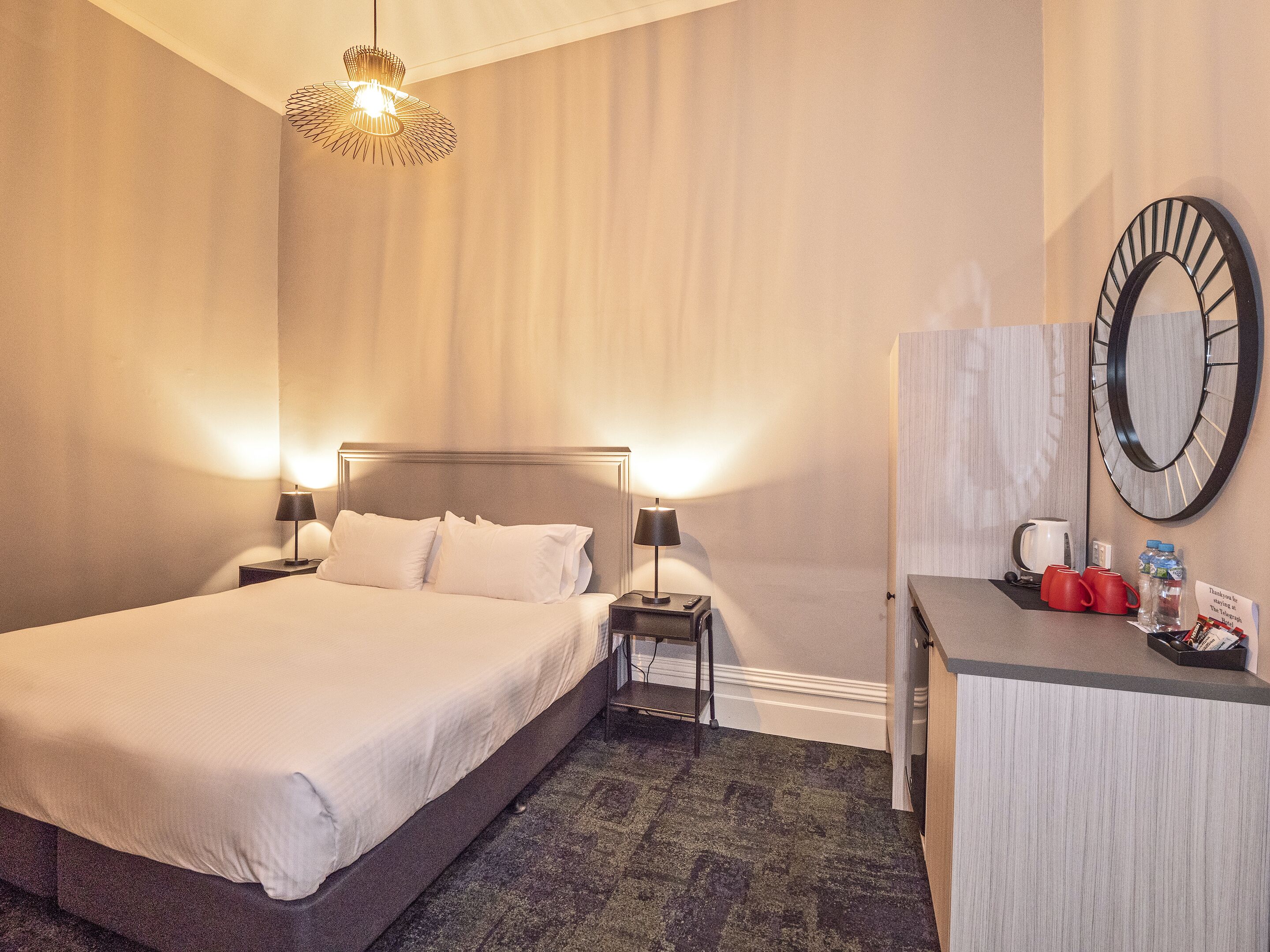 Une chambre d’hôtel équipée d’un lit, de lampes de chevet, d’un bureau avec un miroir et d’une machine à café.