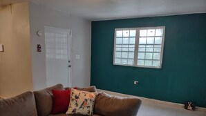 A living room with a brown sofa, a teal accent wall, a window, and a white door. - The Green House in Vega Alta, Zen zone close to the beach (Vega Alta)