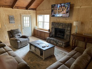 A cozy living room with a stone fireplace, leather sofas, a television, and a sign with 'Lake Rules'. - Crappie Fishing, Hunting, ATV Trails, Boating, Fishing, State Park, Camping (Oakland)