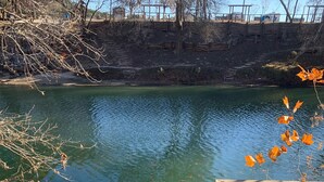 A wooden deck leading to a calm body of water with a wooden railing on one side. - River View Retreat LLC (New Braunfels)