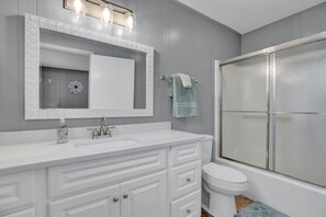 A bathroom with a white vanity, a large mirror, a toilet, and a glass-enclosed shower. - River View Retreat LLC (New Braunfels)