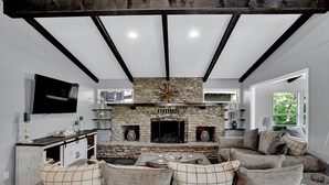 A cozy living room with a stone fireplace, a sofa with patterned cushions, and a flat-screen TV mounted on the wall. - River View Retreat LLC (New Braunfels)