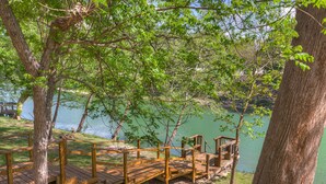 A wooden deck with a staircase leading to a platform over a body of water, surrounded by trees. - River View Retreat LLC (New Braunfels)