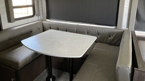 Un intérieur de camping-car compact comprenant un coin repas, une grande fenêtre et des sièges intégrés.
