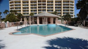 Une piscine avec un kiosque, des palmiers et un hôtel à plusieurs étages en arrière-plan.