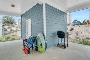 Un espacio al aire libre cubierto con un cobertizo azul, una pelota de playa, una pelota de voleibol, una parrilla y un carrito con una tabla de surf.