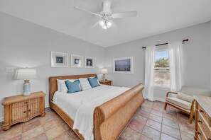 A bedroom with a bed, a chair, a nightstand, a lamp, and a ceiling fan.
