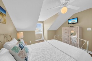 Un dormitorio con una cama, ventilador de techo, televisor y ventana con persianas.