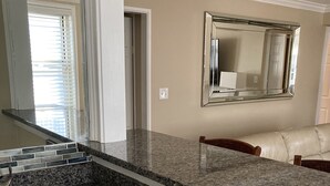 A kitchen with a granite countertop, stainless steel sink, and white cabinetry.
