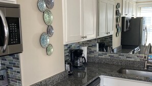 A modern kitchen with white cabinets, a granite countertop, a stainless steel refrigerator, and a microwave.