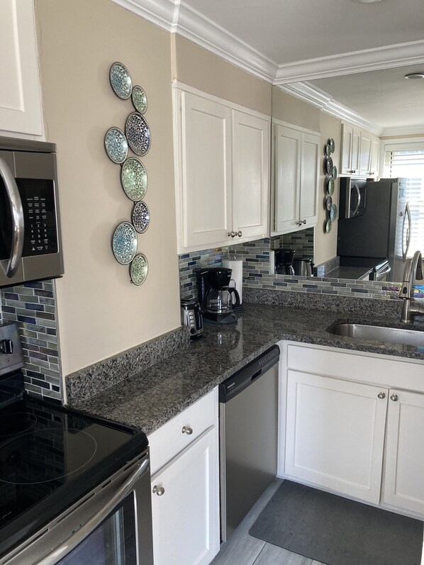 A modern kitchen with white cabinets, a granite countertop, a stainless steel refrigerator, and a microwave.