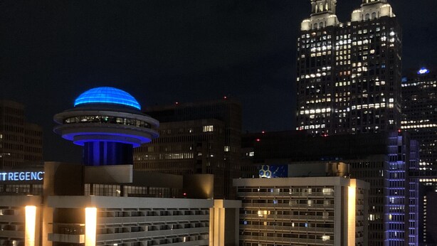 A high-rise building with a distinctive blue-lit dome structure on top, surrounded by other tall buildings with illuminated windows.