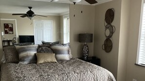 A bedroom with a large bed, two ceiling fans, a TV, and a decorative wall piece.
