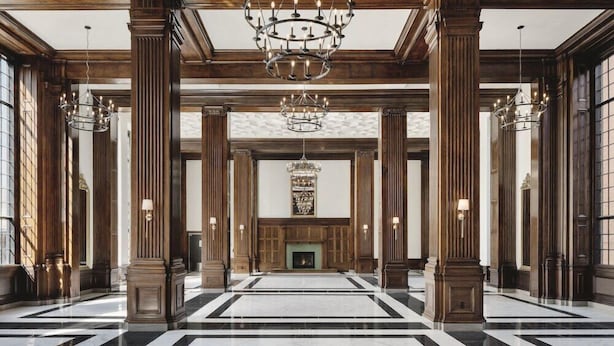 Un vaste hall d’entrée avec de hautes colonnes en bois, un grand lustre et une cheminée.