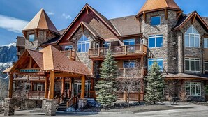 Un bâtiment à étages, de style chalet, doté d’une façade en pierre, de nombreux balcons et d’une entrée imposante avec un porche abrité.