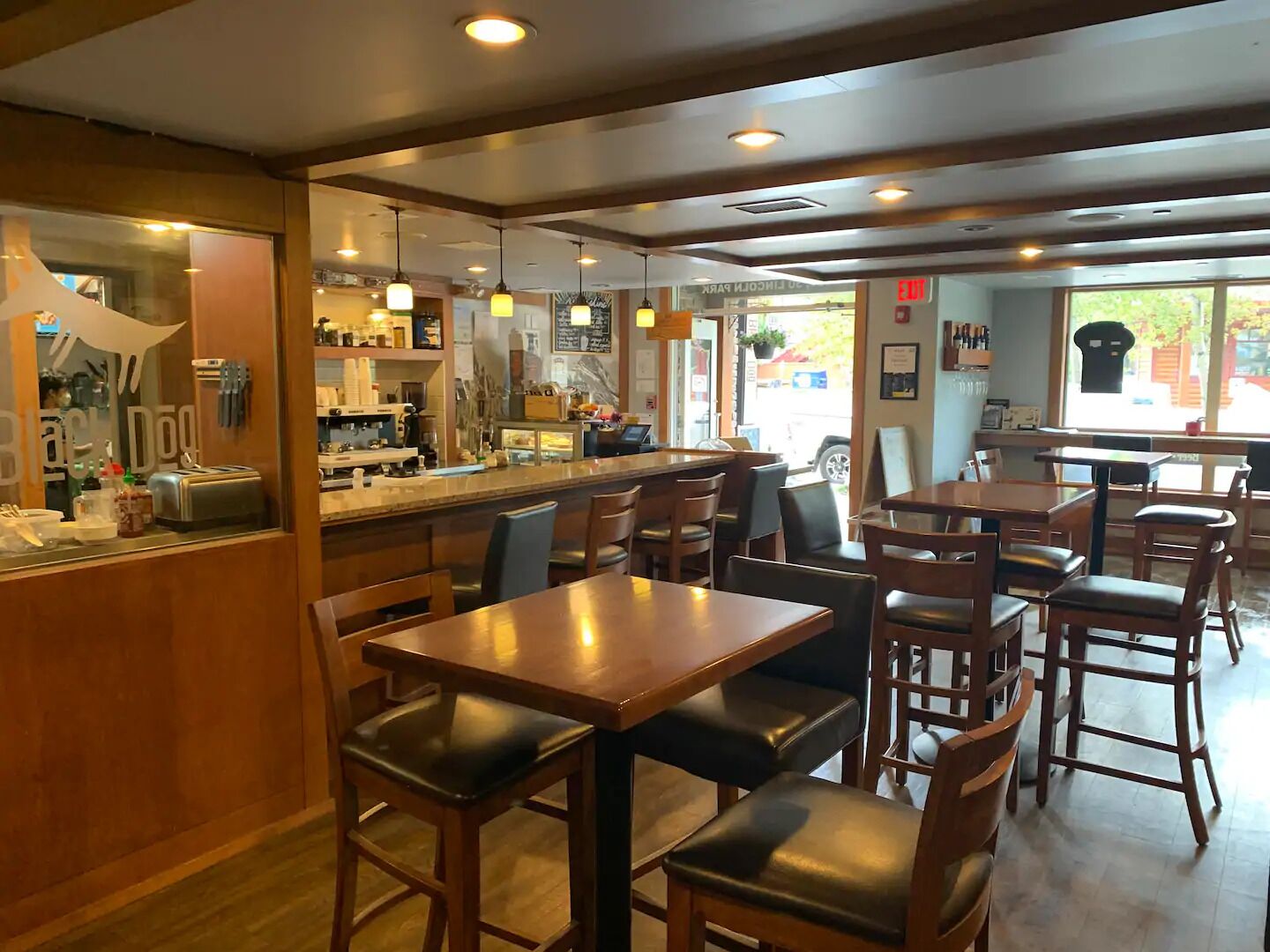 A restaurant interior with wooden tables and chairs, a bar area, and a view of the street outside.