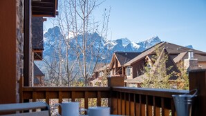 Une terrasse en bois avec une table et des chaises, offrant une vue sur une chaîne de montagnes aux sommets enneigés.