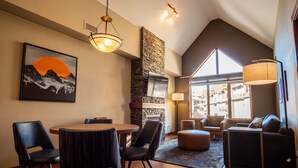 Un salon moderne avec une cheminée en pierre, un coin repas avec des chaises, un canapé et une grande fenêtre donnant sur la ville.