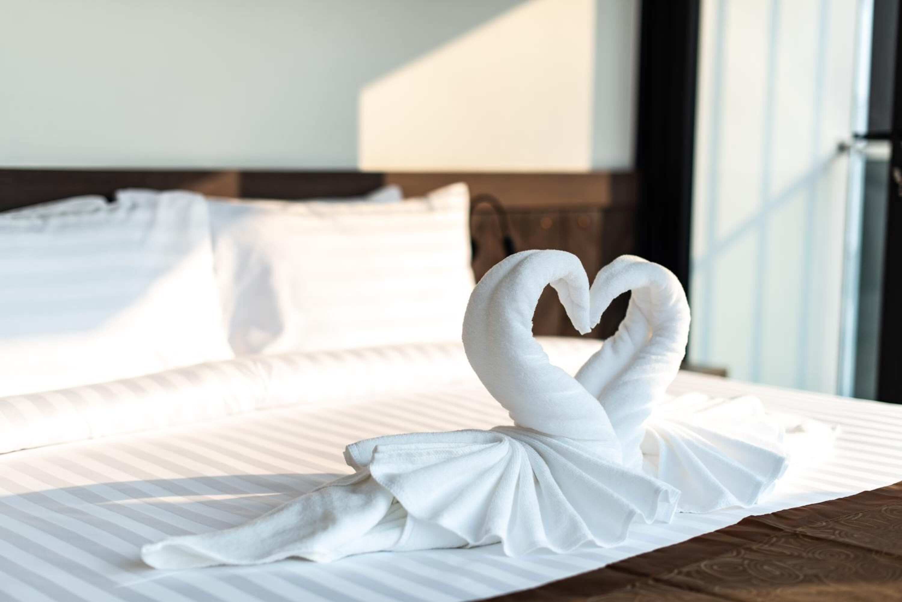 A bed with white linens and a towel arranged in a heart shape on the bed.